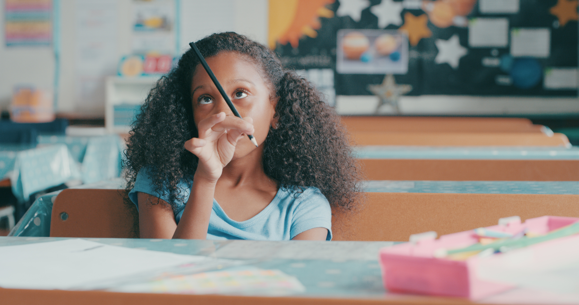 Shot of a young girl looking bored while playing at a school desk