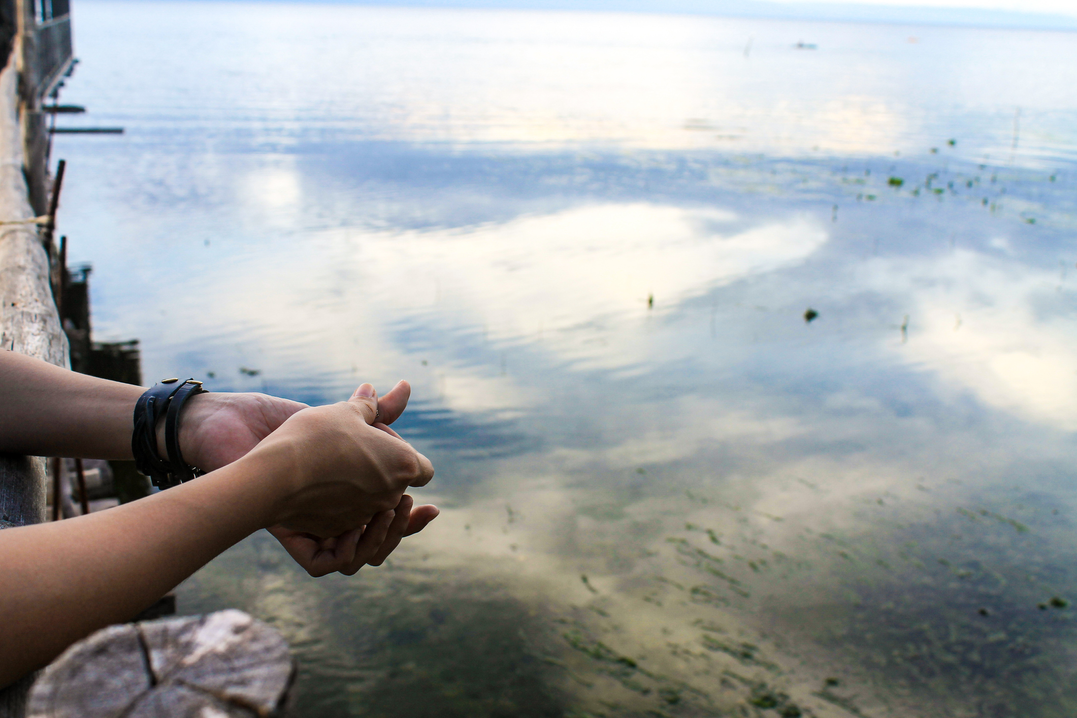 Hands clasped over water reflecting clouds.